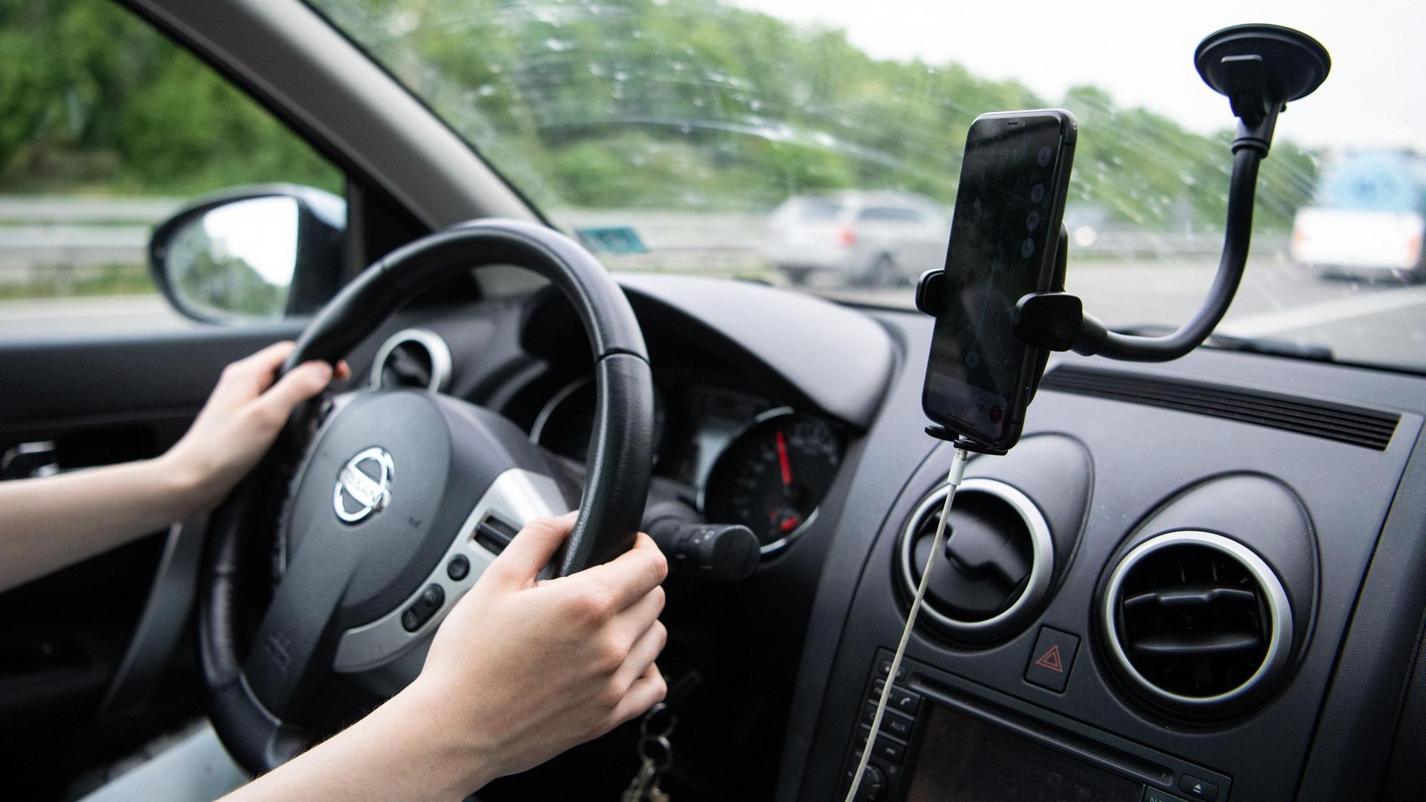 Eine Frau sitzt im Auto mit einem Smartphone in einer Halterung.