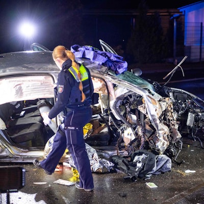 Eine Polizistin geht im Dunkeln an einem zerstörten Auto vorbei.
