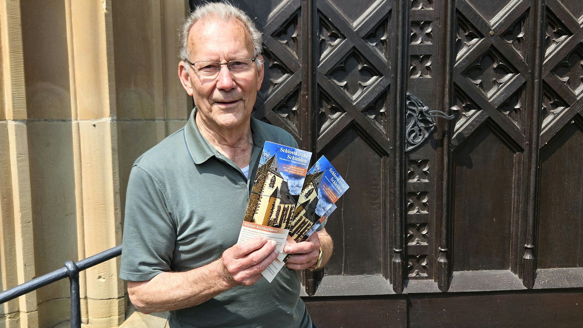 Heinrich Vaßen steht vor der Kirchentür und hält einige Flyer in den Händen.