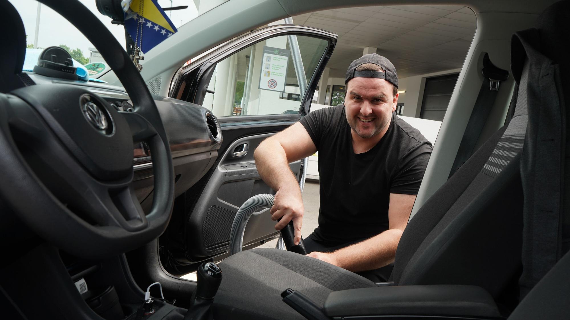 Das Foto zeigt einen Mann, der den Innenraum seines Autos saugt.