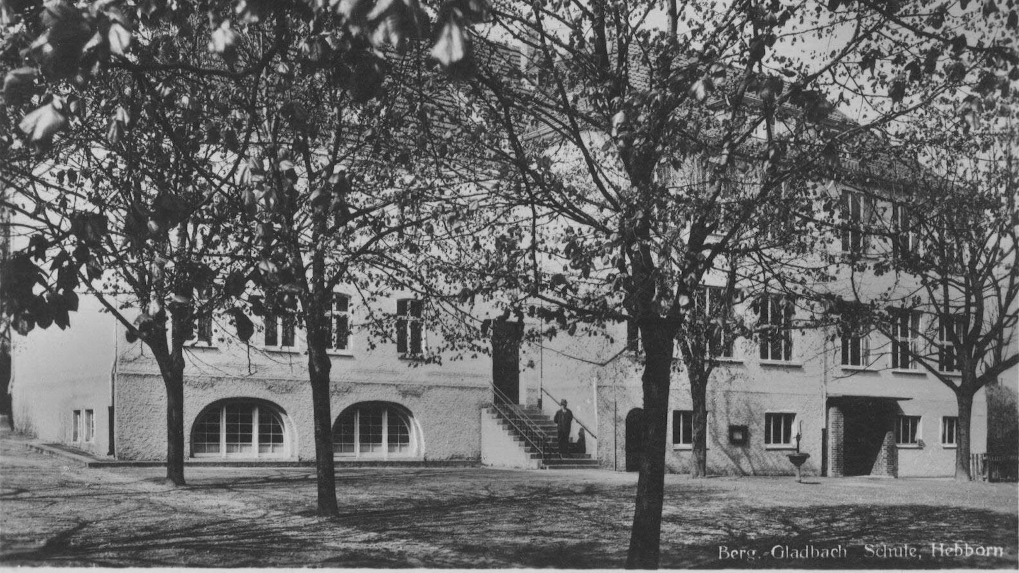 Eine historische Ansichtskarte zeigt ein altes Schulgebäude. Aufschrift: „Berg.-Gladbach Schule, Hebborn“
