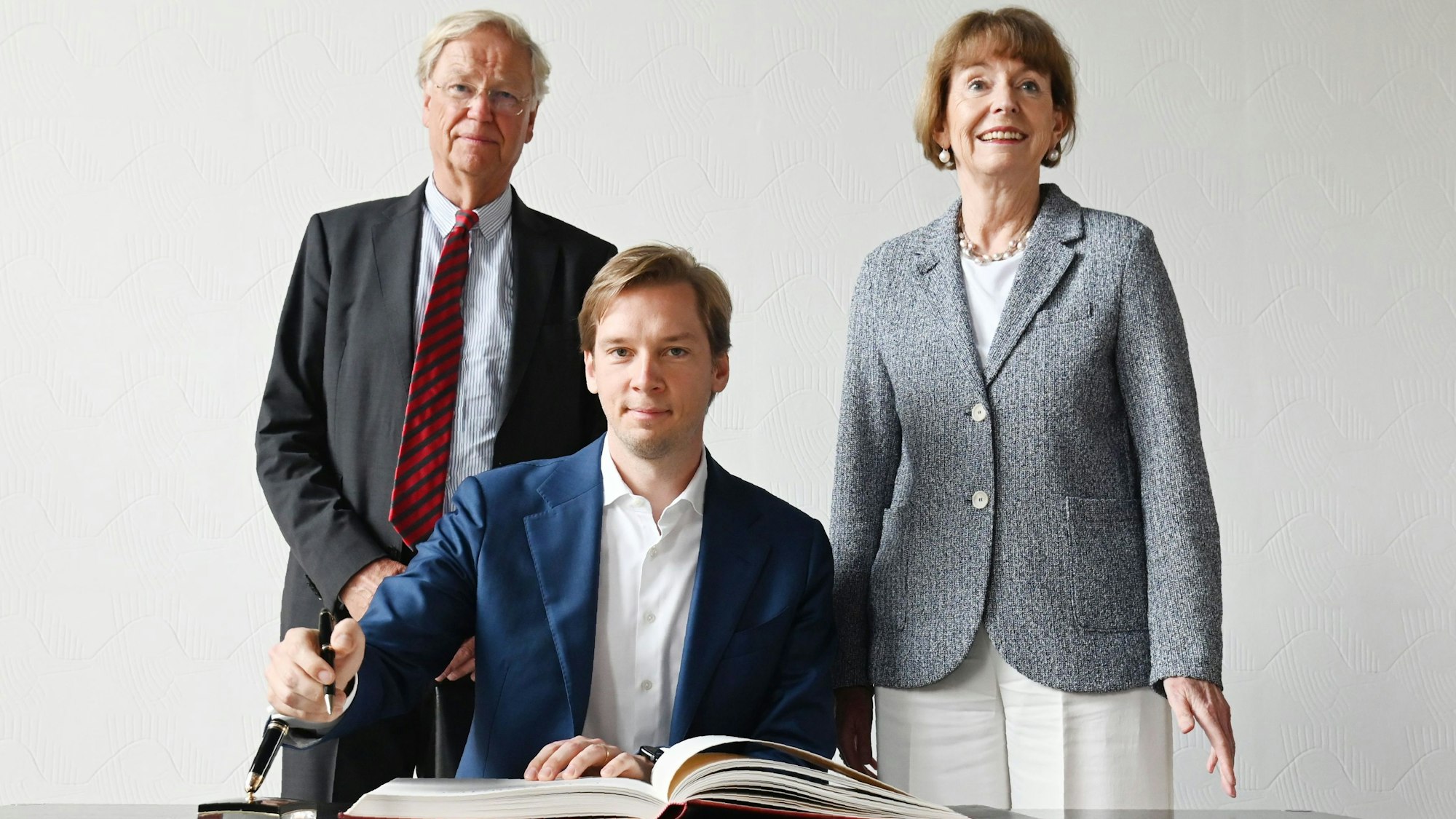 Max (sitzend) und Franz-Georg Heggemann tragen sich in das Gästebuch der Stadt Köln ein. Rechts von ihnen steht Henriette Reker.