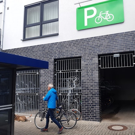 Das Foto zeigt einen Mann, der ein Rad vor einer Fahrradgarage schiebt.