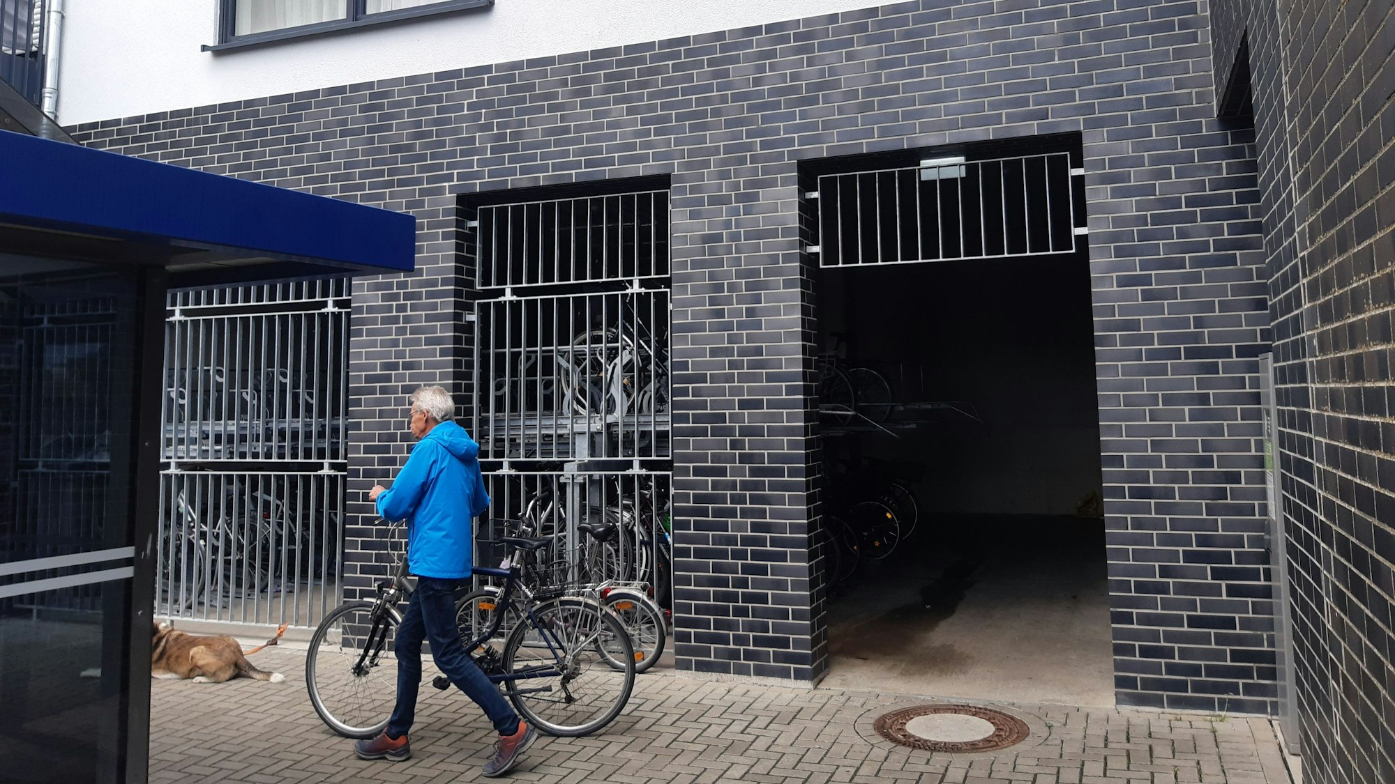 Das Foto zeigt einen Mann, der ein Rad vor einer Fahrradgarage schiebt.