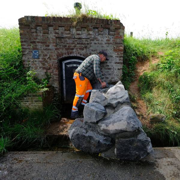 Ein Mitarbeiter des Bauhofs mit orangefarbener Arbeitshose und kariertem Hemd an der nun mit großen Natursteinblöcken verschlossenen Quelle in Lessenich.