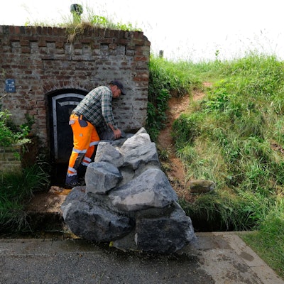 Ein Mitarbeiter des Bauhofs mit orangefarbener Arbeitshose und kariertem Hemd an der nun mit großen Natursteinblöcken verschlossenen Quelle in Lessenich.