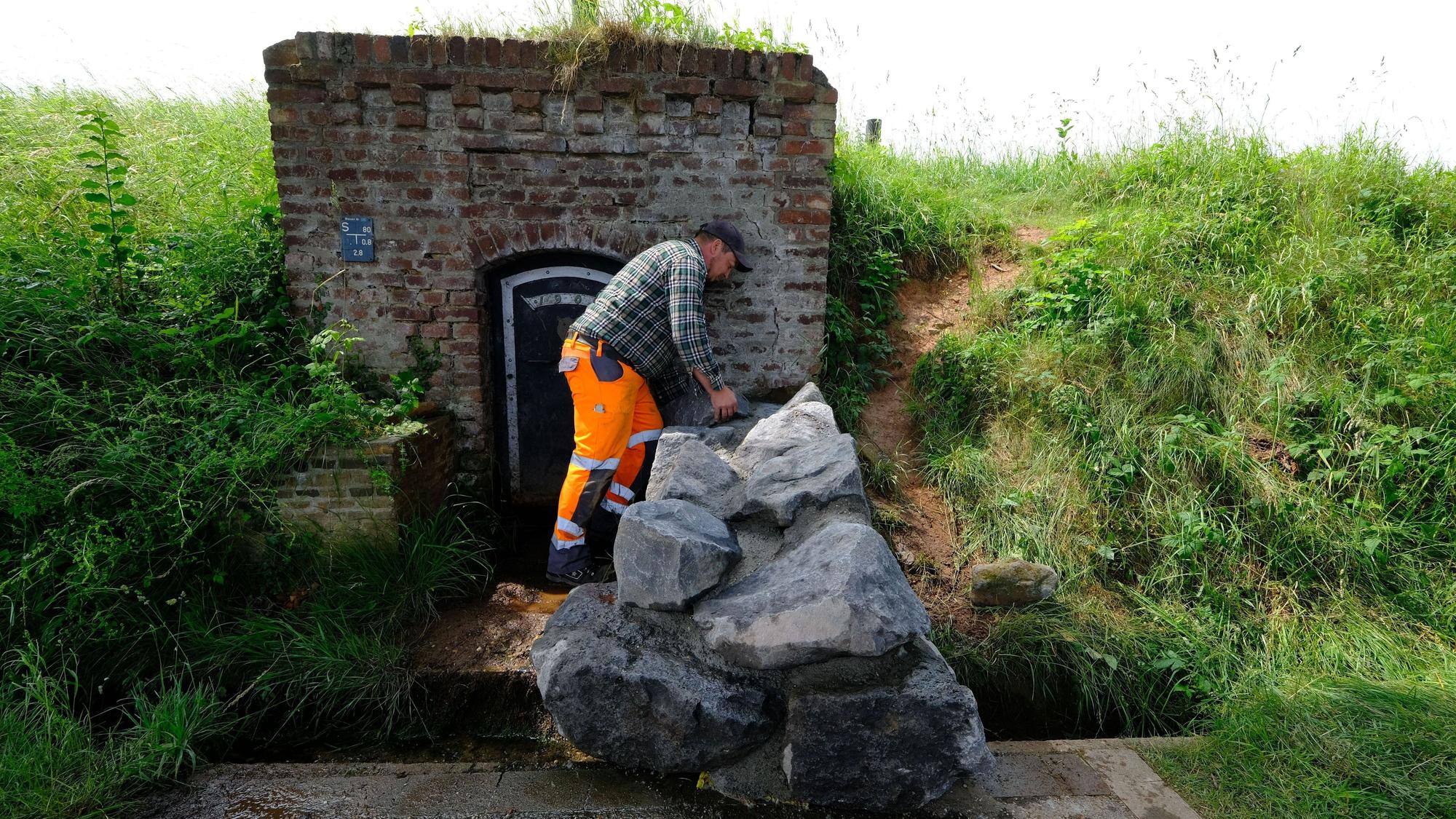 Ein Mitarbeiter des Bauhofs mit orangefarbener Arbeitshose und kariertem Hemd an der nun mit großen Natursteinblöcken verschlossenen Quelle in Lessenich.