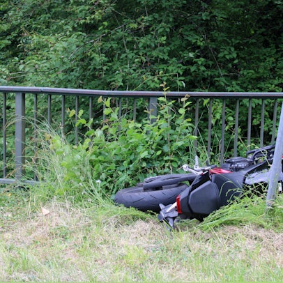 Ein verunfalltes Motorrad (Honda) liegt in einer Wiese neben einem Geländer in Odenthal-Altenberg.