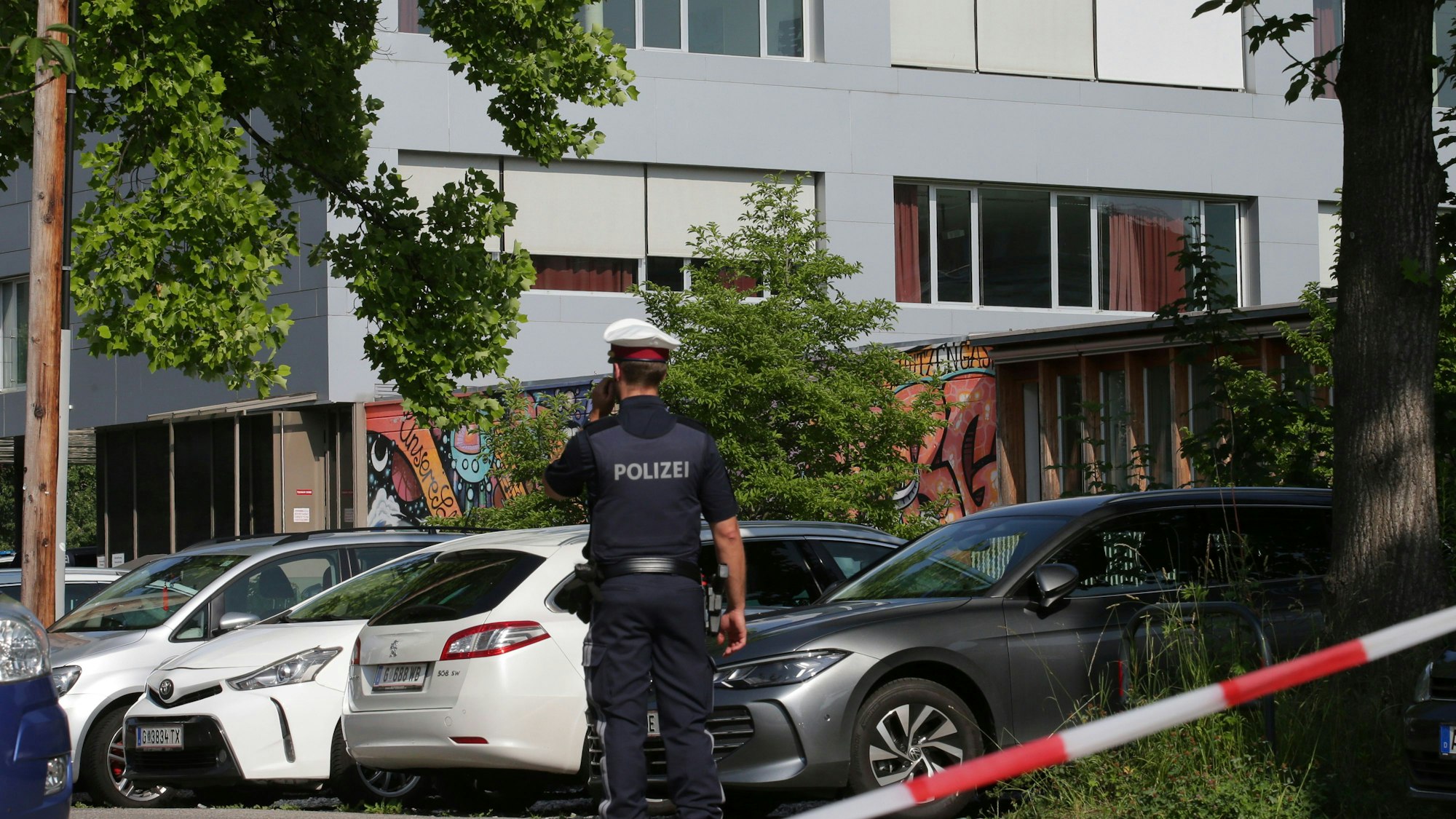 Ein Polizeibeamter telefoniert vor dem Schulgebäude. Ein 21-Jähriger aus dem Raum Graz hat nach Angaben der Behörden die tödlichen Schüsse an einem Gymnasium im österreichischen Graz abgegeben.