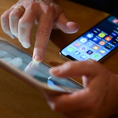 Eine Person tippt auf ein iPad, vor ihr liegt ein Smartphone auf dem Tisch