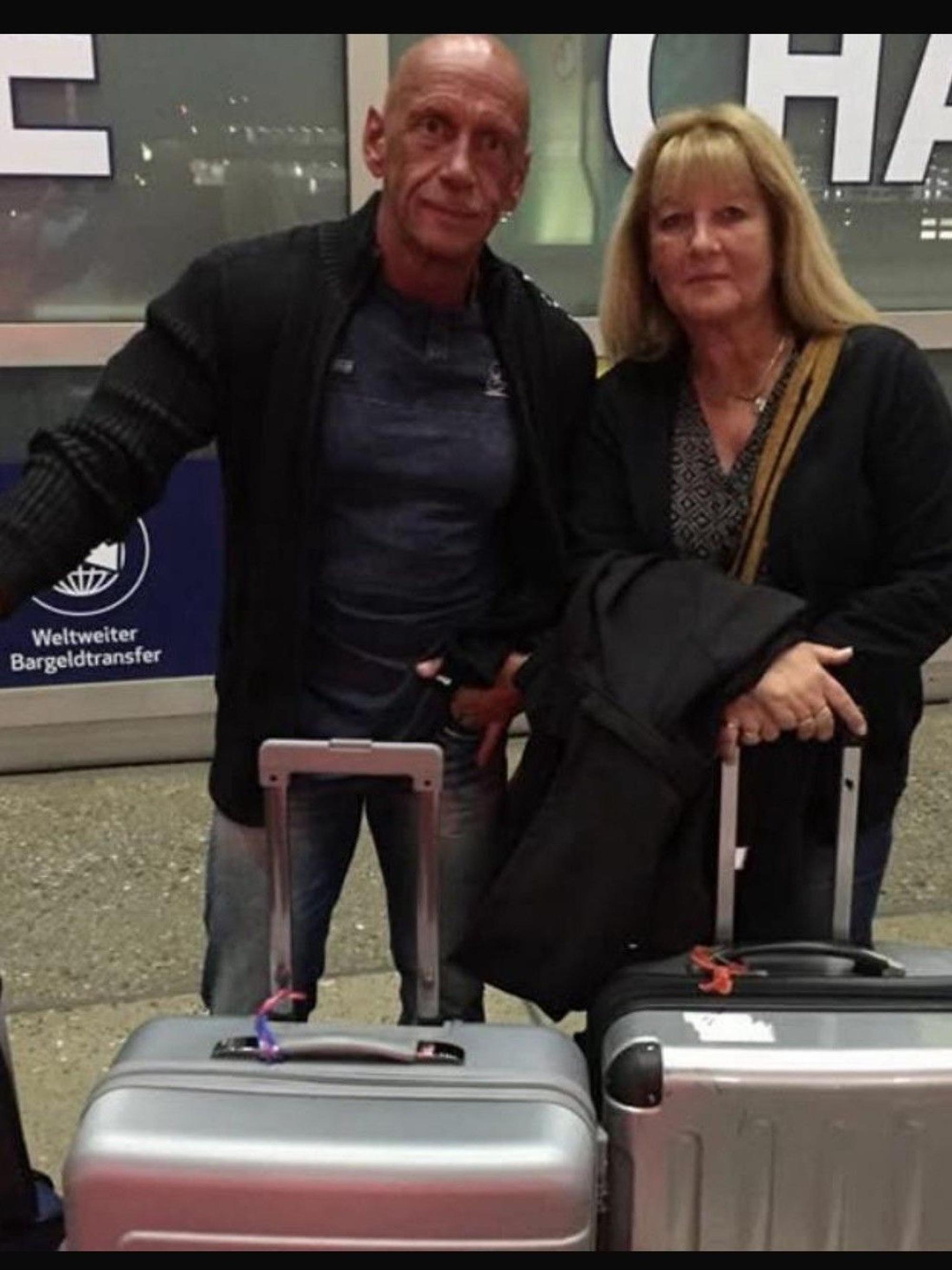 Auf dem Bild ist das Ehepaar mit Koffern am Flughafen zu sehen.