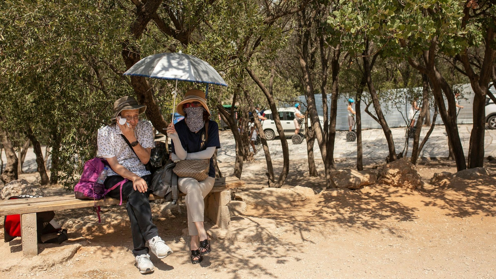Touristen sitzen unter Bäumen am Eingang der Akropolis in Athen.