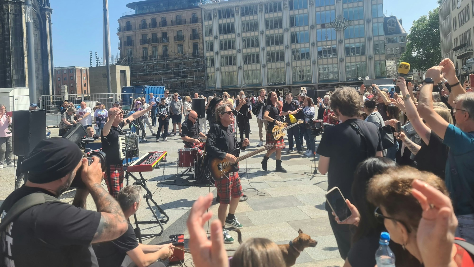 Zu sehen sind viele Menschen, die auf der Domplatte vor der Band Brings stehen, die gerade ein Konzert geben.