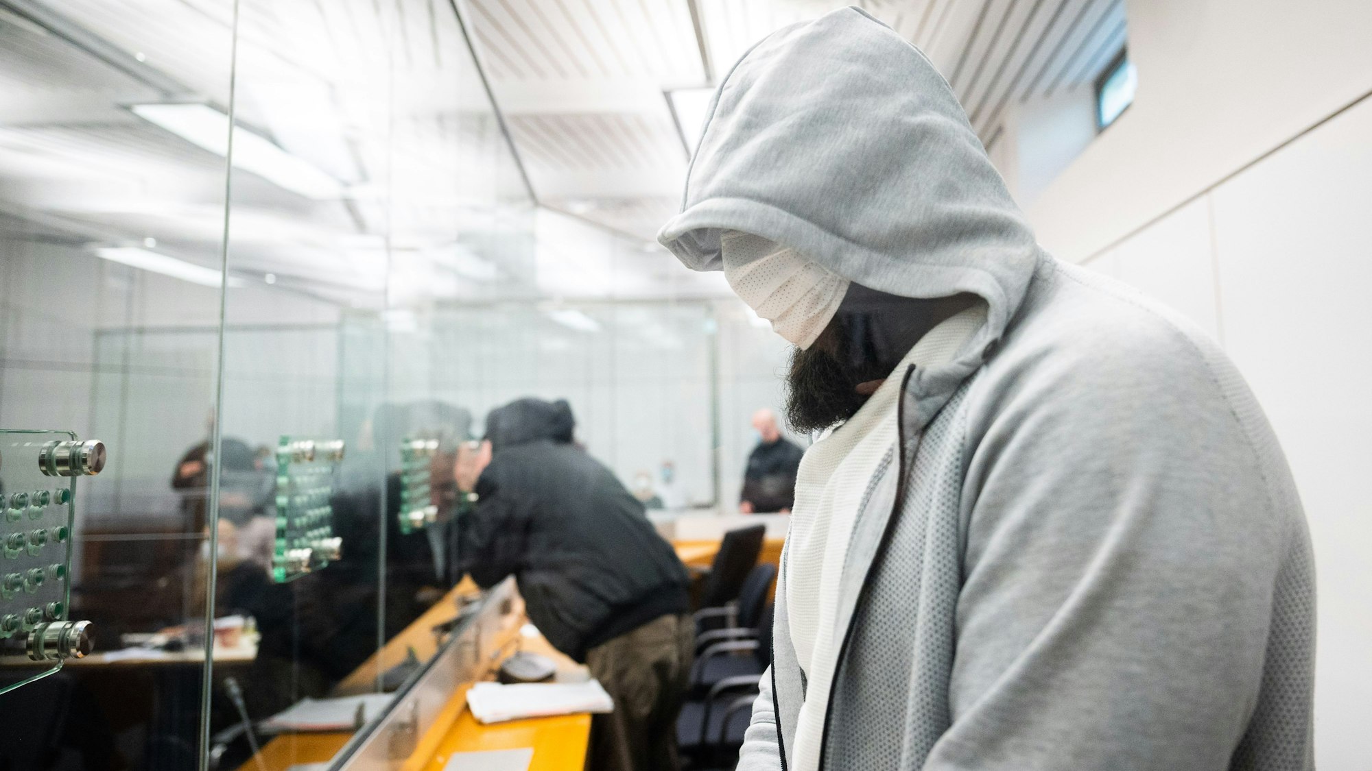 Abu Walaa (vorn), mutmaßlicher Anführer der Terrormiliz Islamischer Staat (IS) in Deutschland, steht im Oberlandesgericht hinter einer Glasscheibe. Foto: Julian Stratenschulte/dpa Pool/dpa