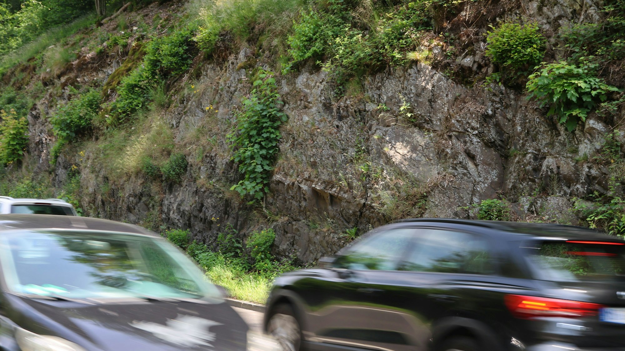 Eine Felswand, davor vorbeifahrende Autos.