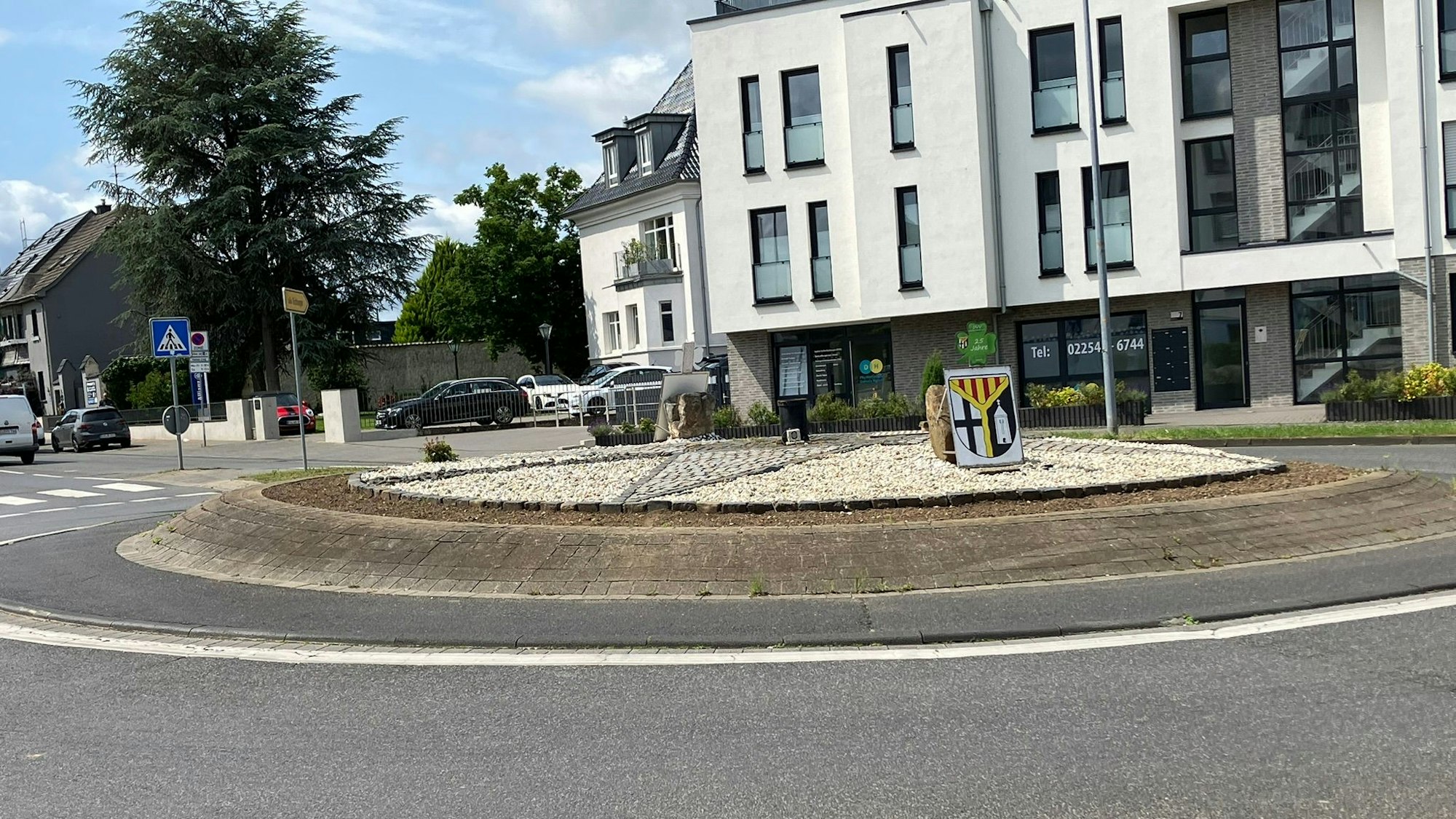 Auf dem Verkehrskreisel in Weilerswist steht ein Wappen. Es liegen Schottersteine auf Fläche inmitten der Straße.