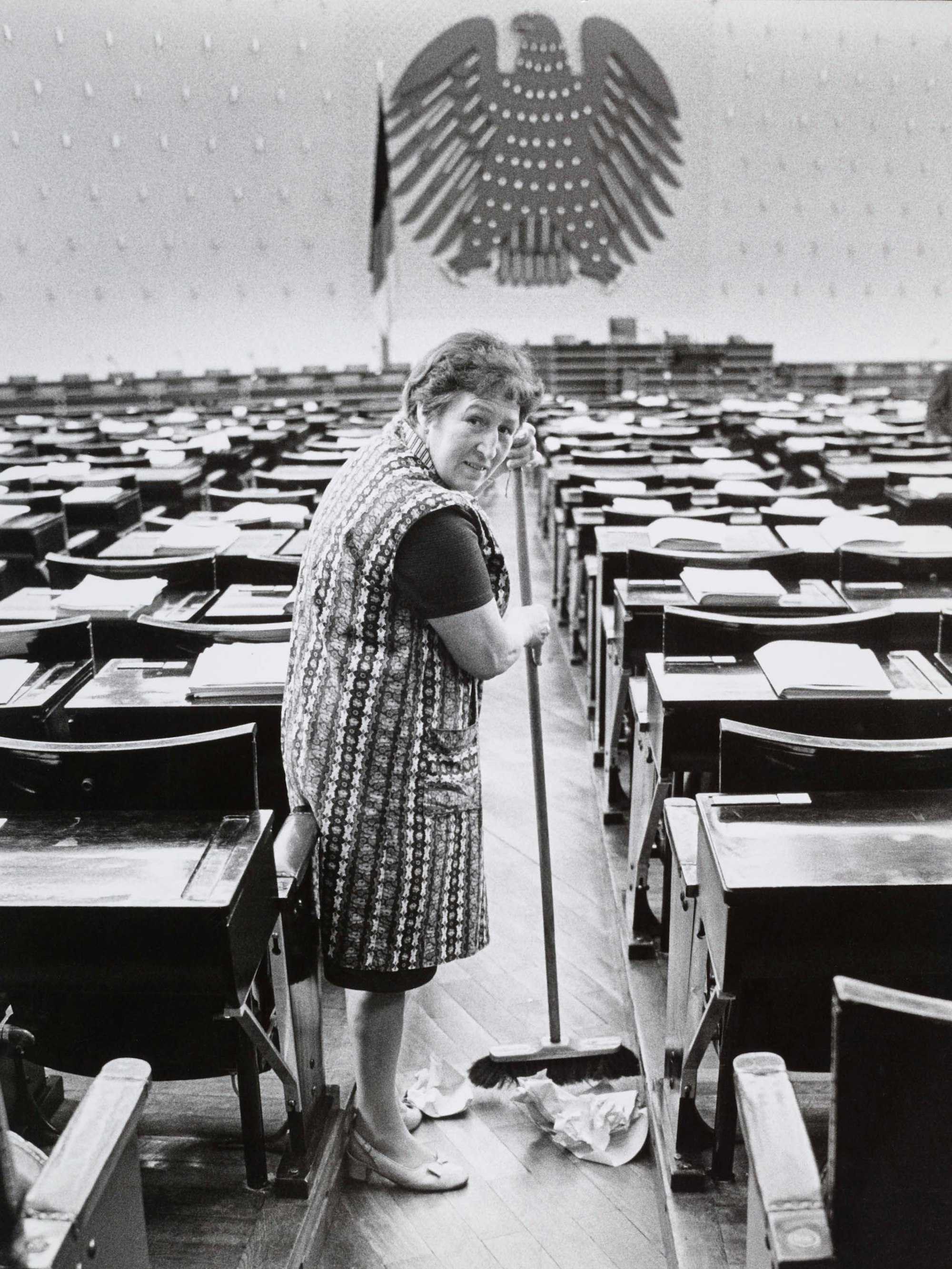 Eine Putzfrau steht im Kittel im leeren Plenarsaal.