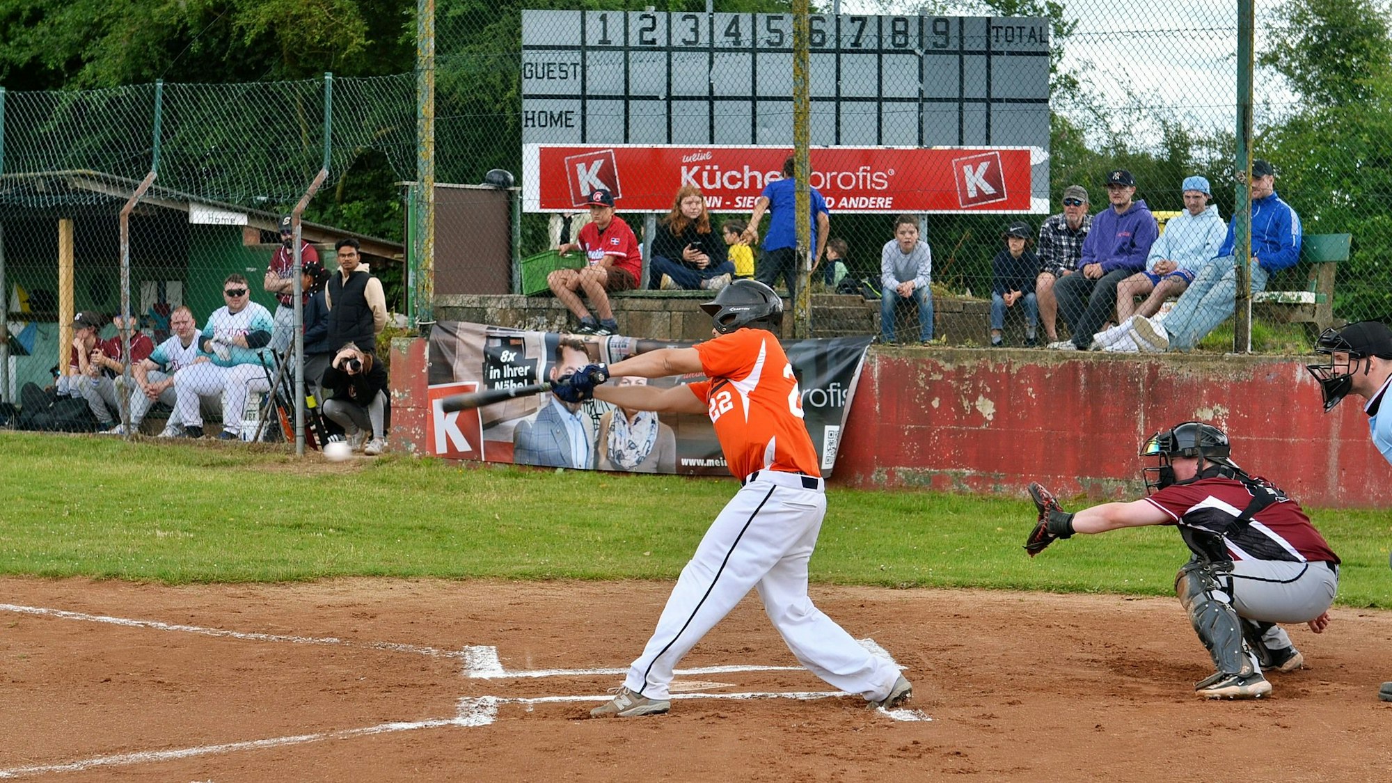 Ein Batter trifft einen Baseball. Der Catcher hinter ihm hat den Handschuh zum Fangen geöffnet.