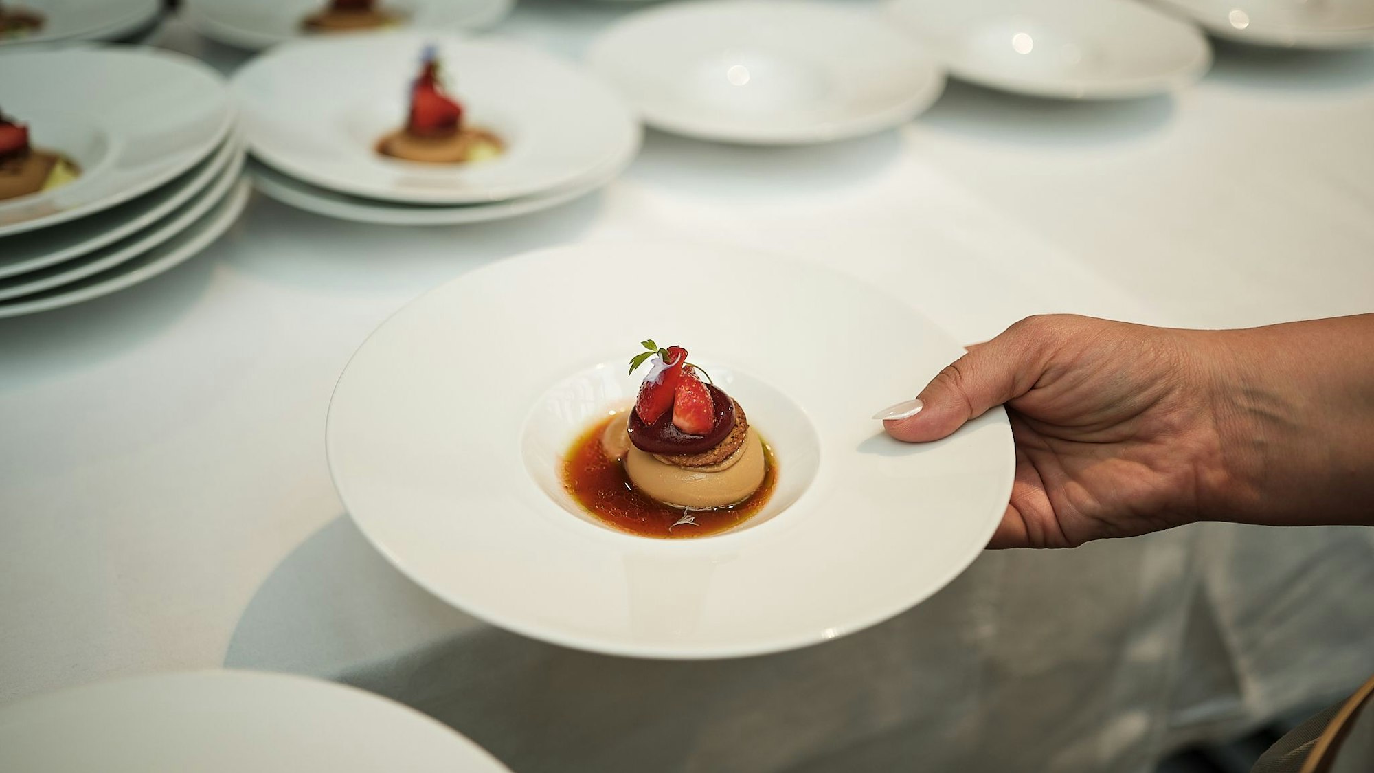 Ein Dessertteller, gehalten von einer Hand, mit einem Nachtisch darin, der mit Erdbeeren belegt ist.