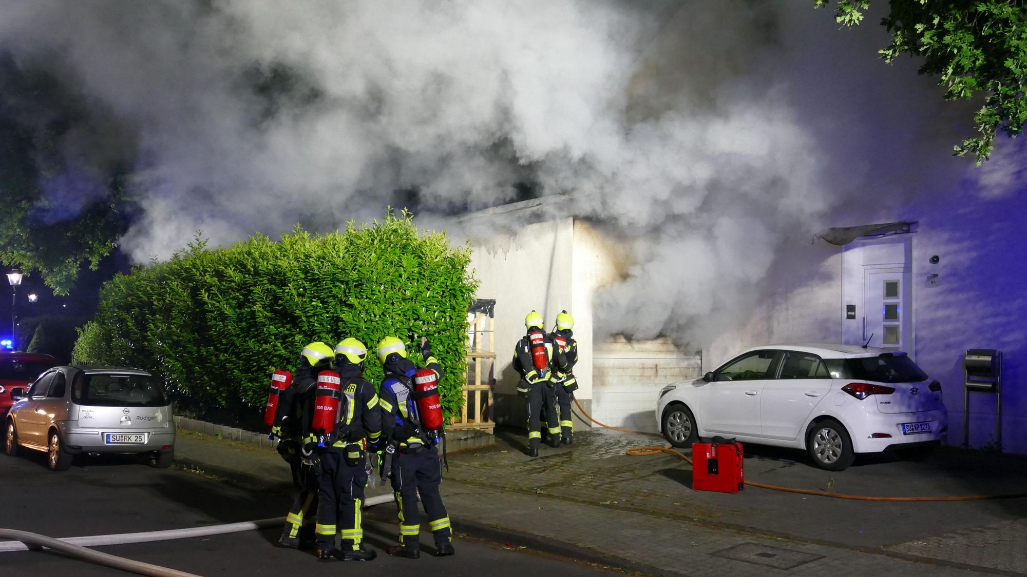 Die Feuerwehr steht vor einem Einfamilienhaus, die Garage brennt.