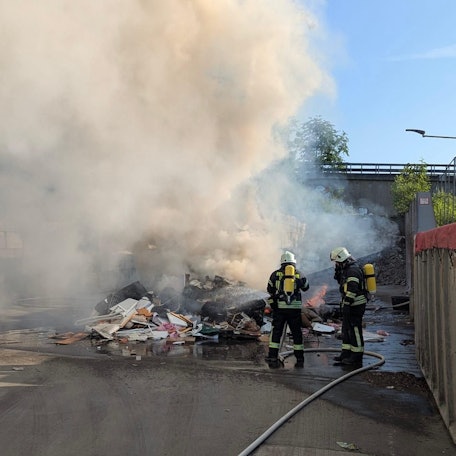 Feuerwehrleute löschen einen brennenden Müllhaufen.