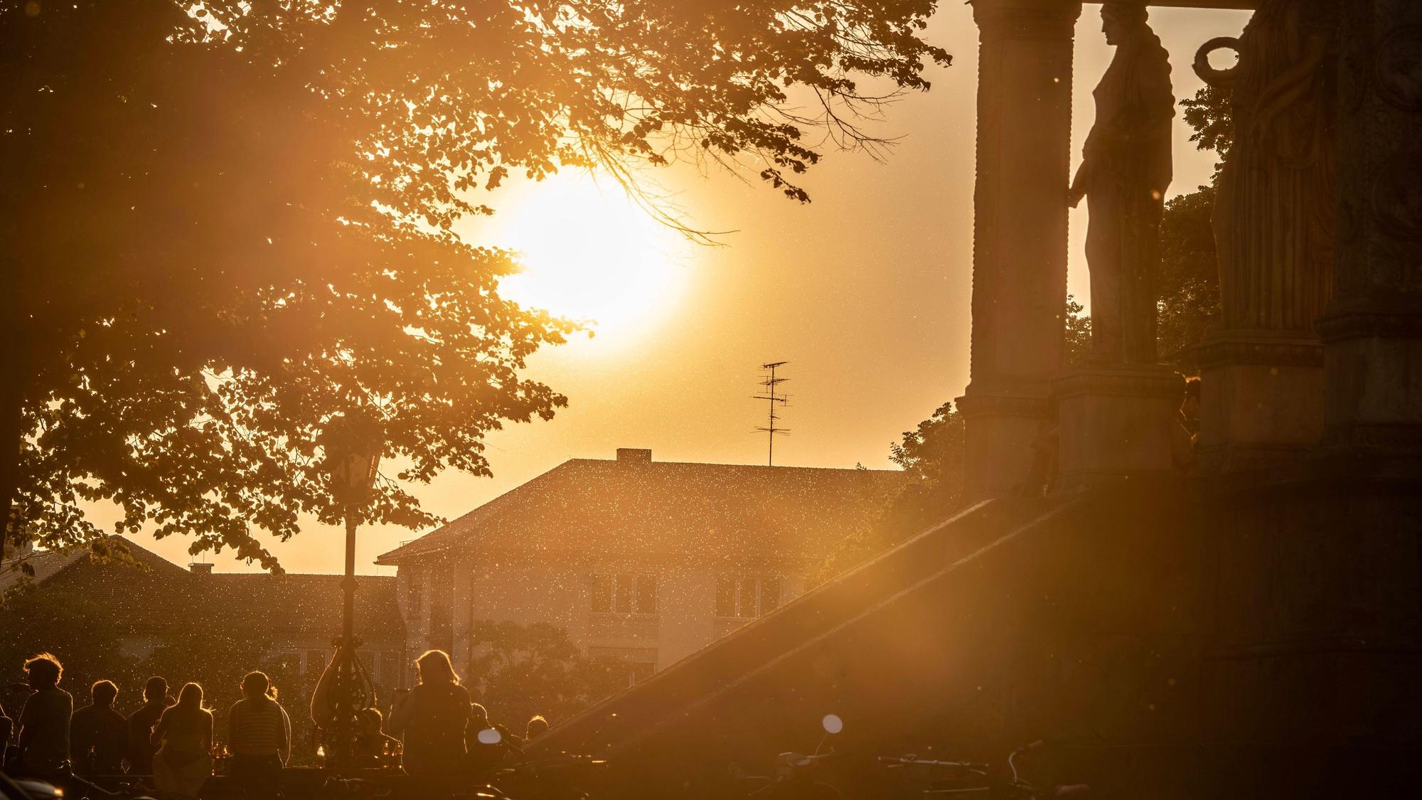 Treffpunkt Friedensengel, junge Menschen genießen den Sonnenuntergang auf der Aussichtsplattform, ein milchiger roter Schleier trübt den Himmel ein, München, Juni 2025