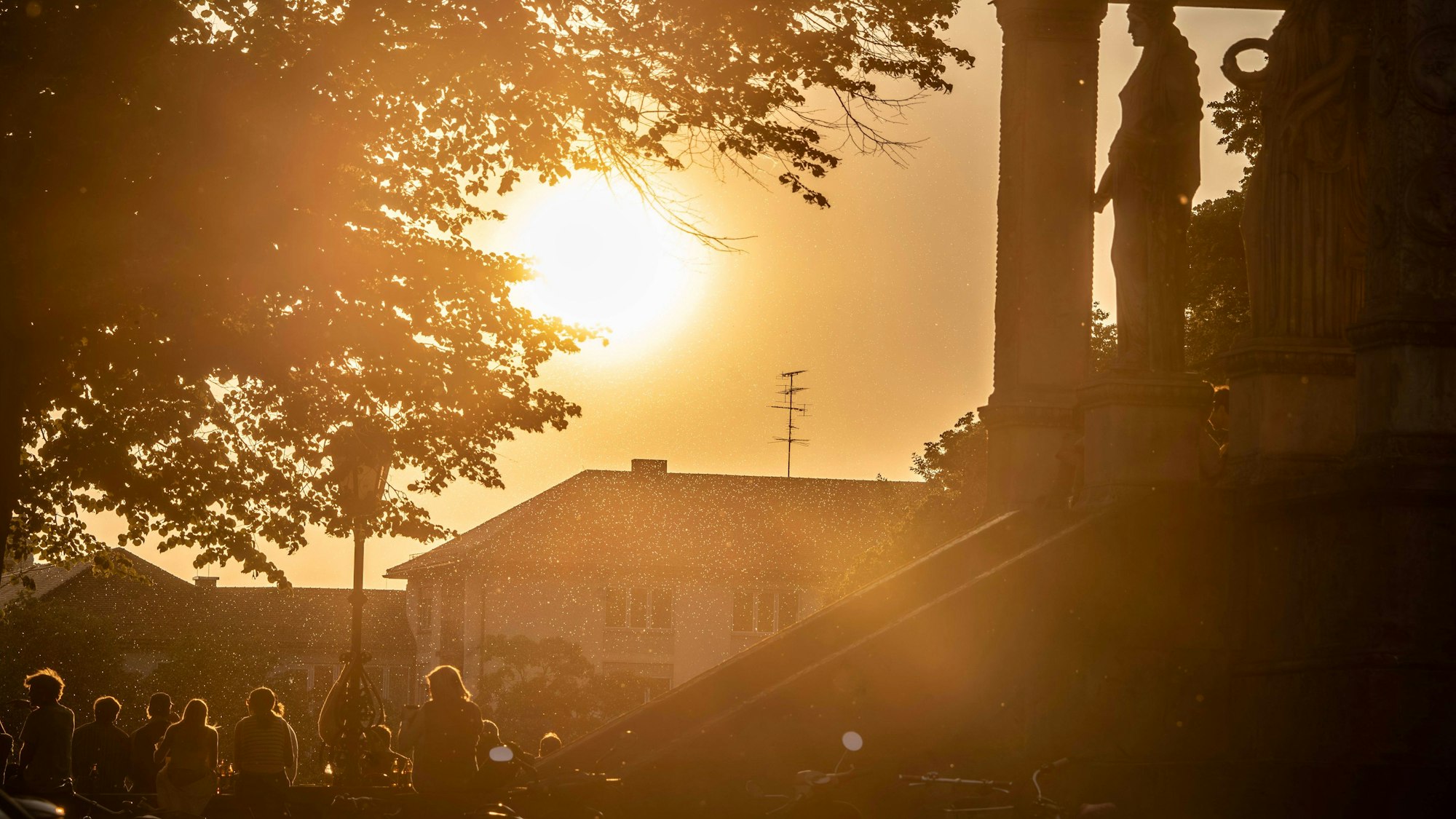 Treffpunkt Friedensengel, junge Menschen genießen den Sonnenuntergang auf der Aussichtsplattform, ein milchiger roter Schleier trübt den Himmel ein, München, Juni 2025