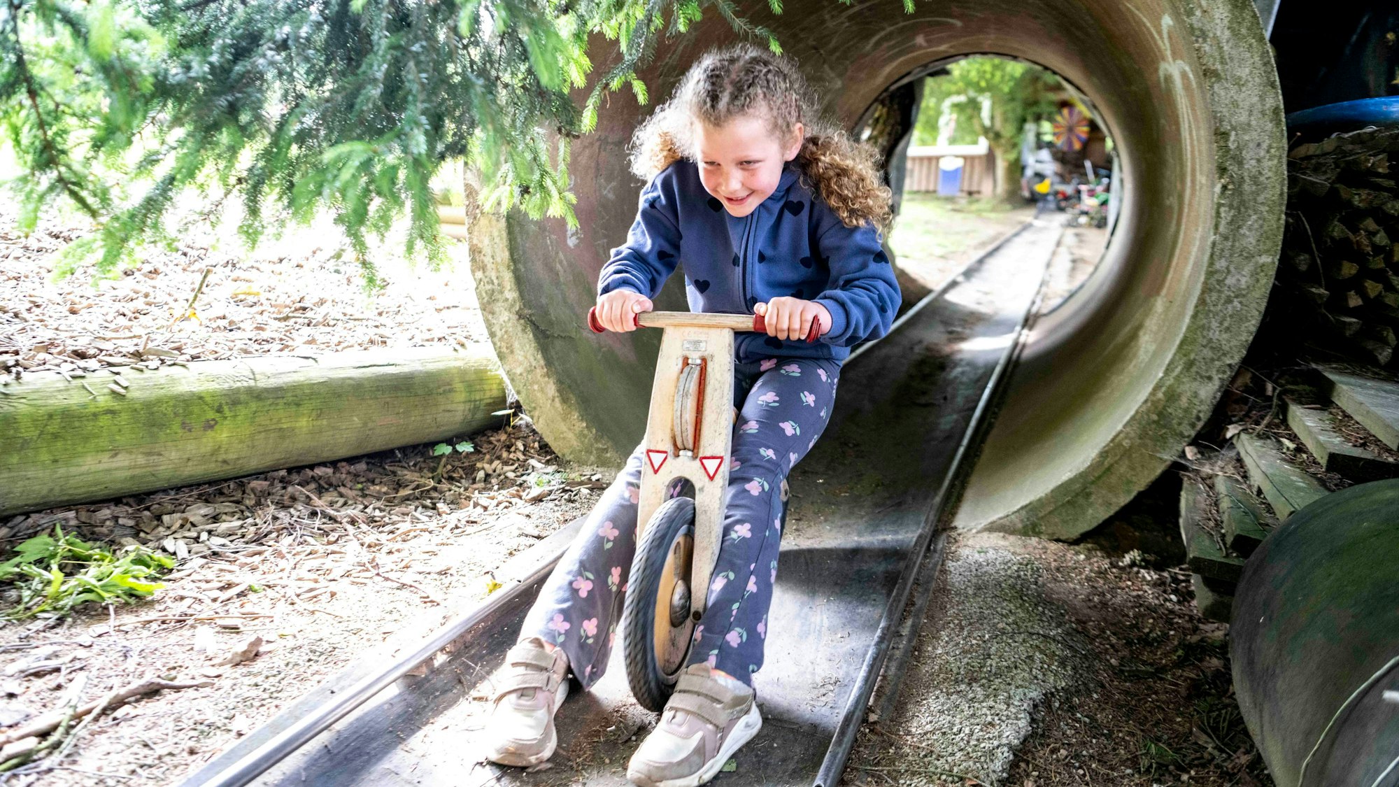 Das Bild zeigt ein Mädchen, das mit einem Laufrad durch ein Rohr fährt.