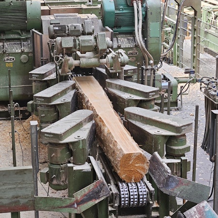 Blick auf eine Maschine mit einem Stamm, an dem an einer Seite die Rinde bereits abgeschnitten wurde.