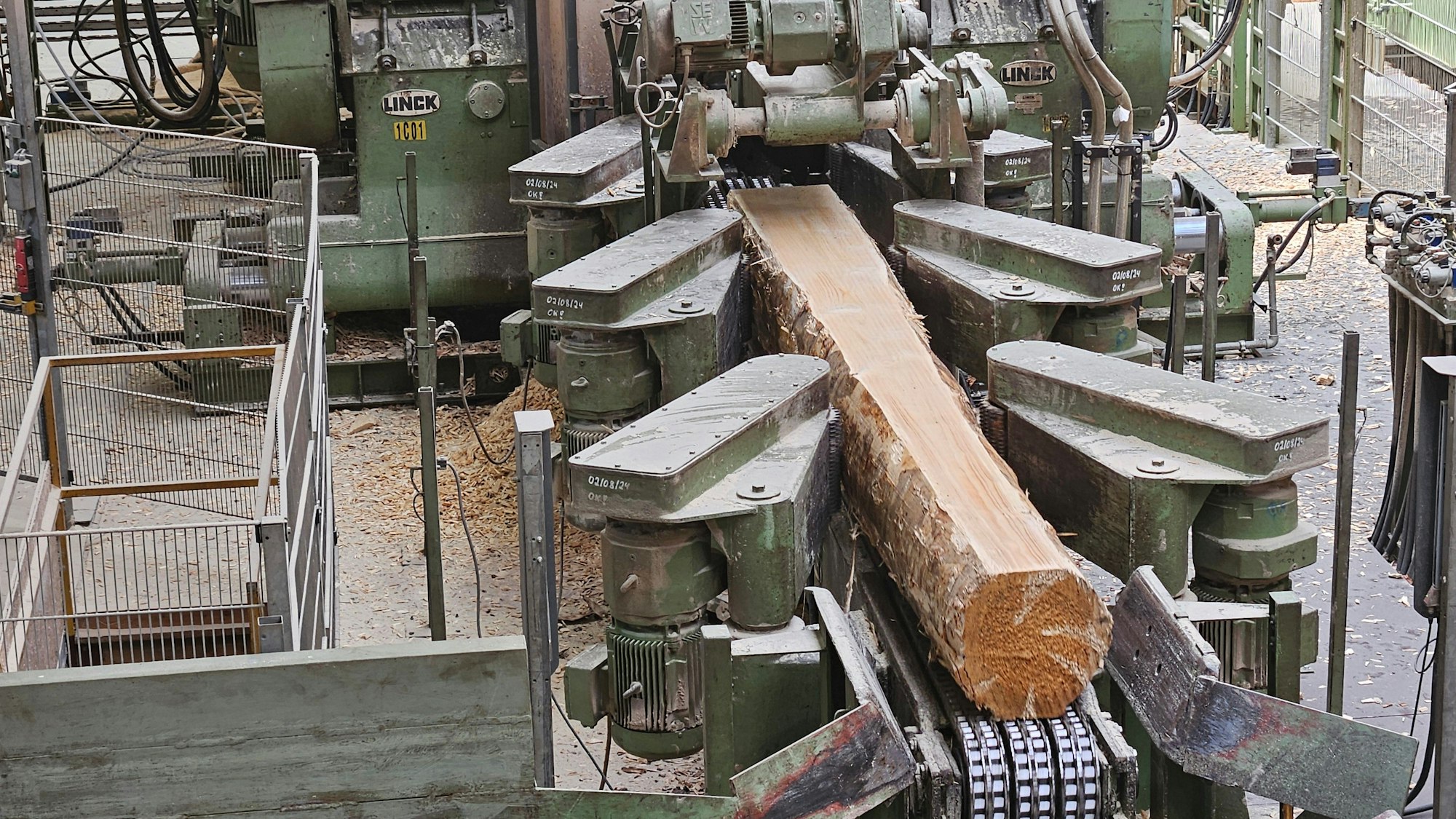 Blick auf eine Maschine mit einem Stamm, an dem an einer Seite die Rinde bereits abgeschnitten wurde.
