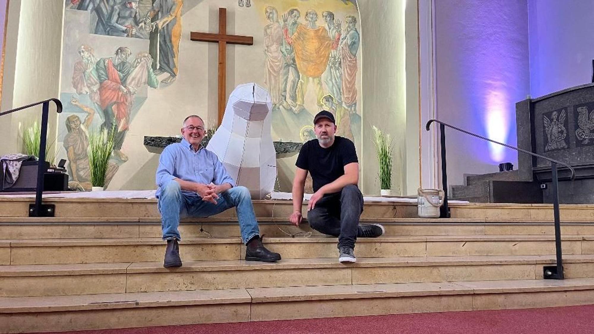 Zwei Männer sitzen auf den Stufen eines Altars, zwischen den beiden die Friedenstaube.