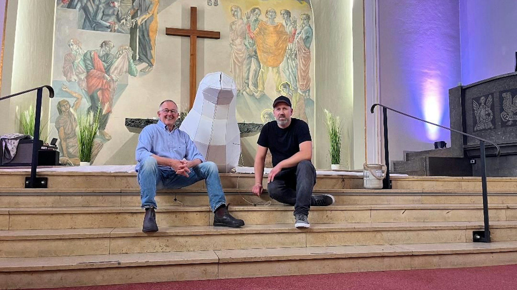 Zwei Männer sitzen auf den Stufen eines Altars, zwischen den beiden die Friedenstaube.