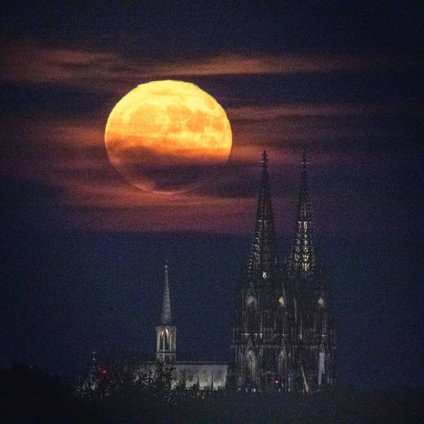 Ein gelblich-rötlicher Vollmond steht über dem Kölner Dom. Das seltene Phänomen wird auf „Erdbeermond“ genannt.