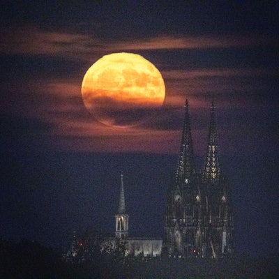 Ein gelblich-rötlicher Vollmond steht über dem Kölner Dom. Das seltene Phänomen wird auf „Erdbeermond“ genannt.