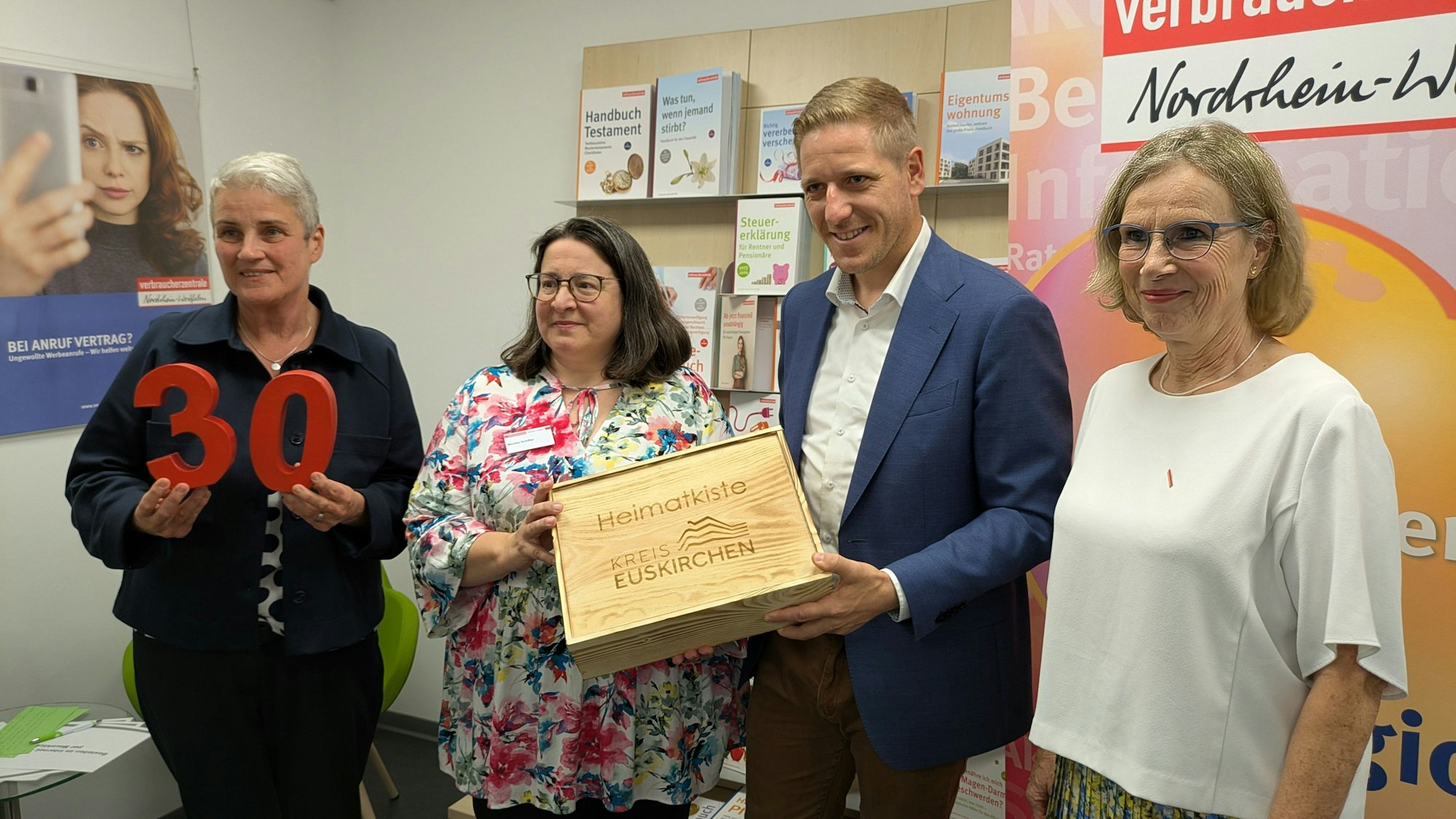 Die Vertreterinnen der Verbraucherzentrale und Markus Ramers stehen nebeneinander. Ramers hält eine Geschenkkiste in den Händen.