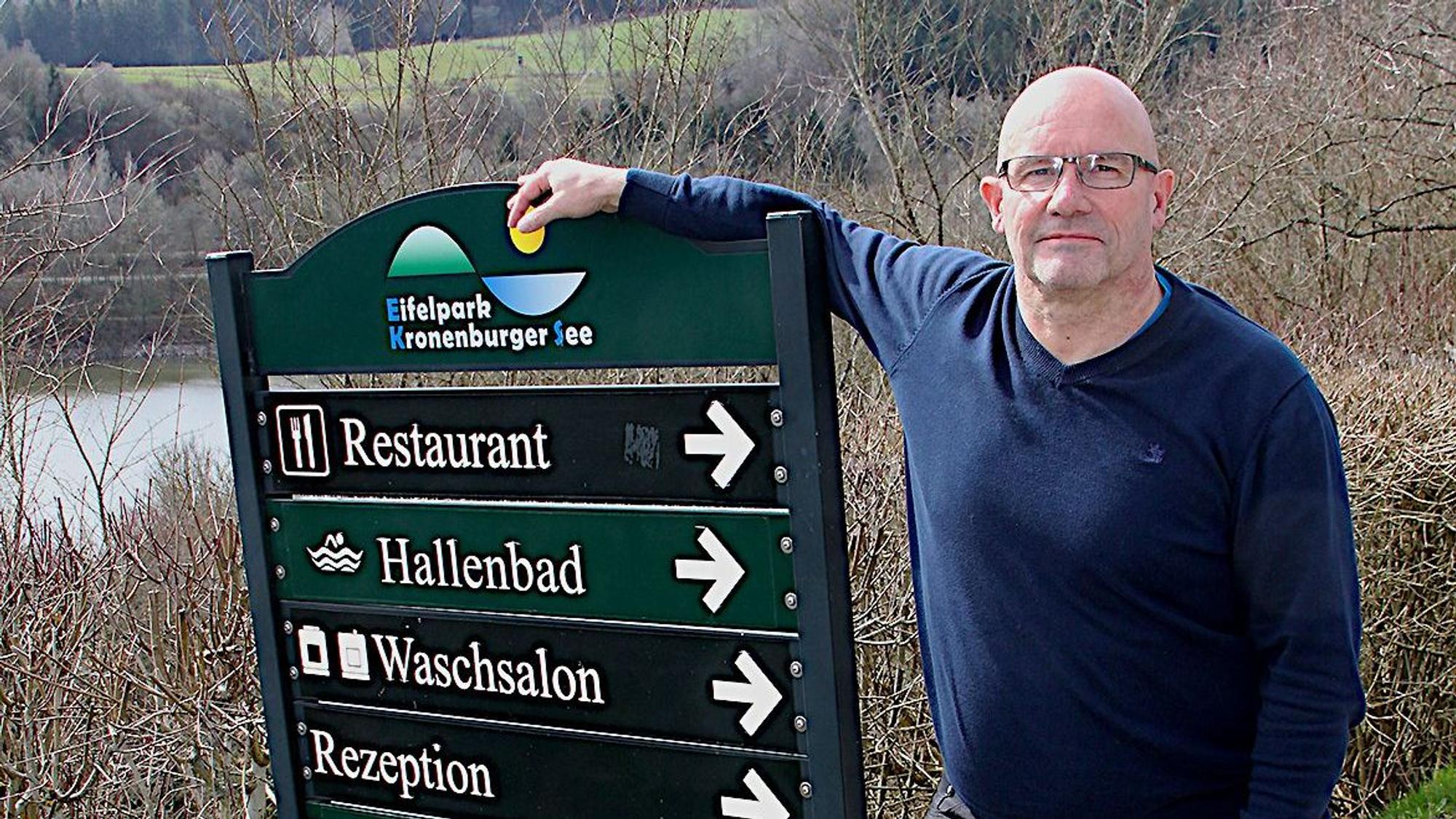 Das Bild zeigt einen Mann, der sich auf eine Hinweistafel mit Wegweisern des Ferienparks stützt.