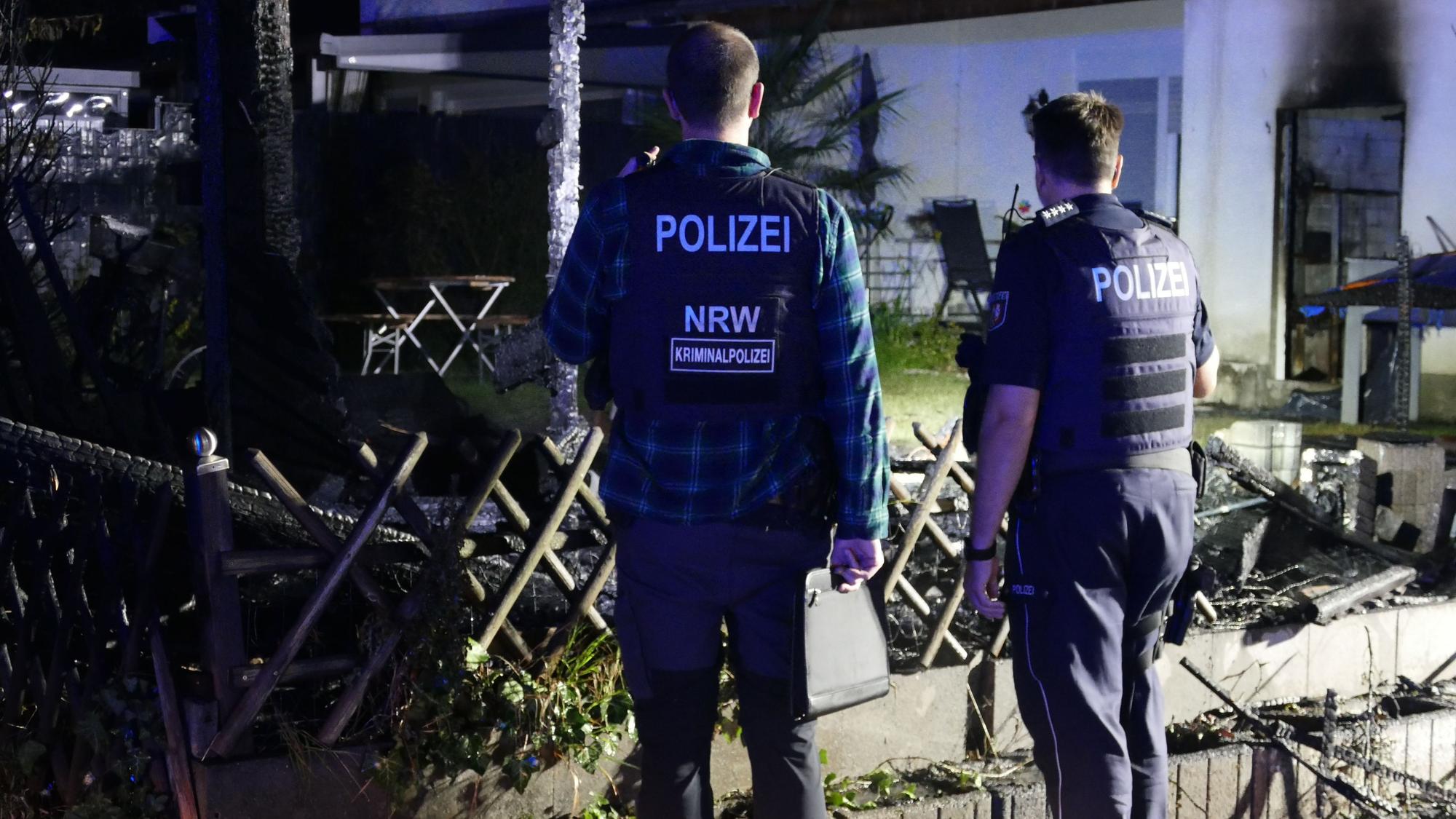 Polizisten der Kripo begutachten die Brandstelle. Von der Hütte sind nur verkohlte Reste übrig.