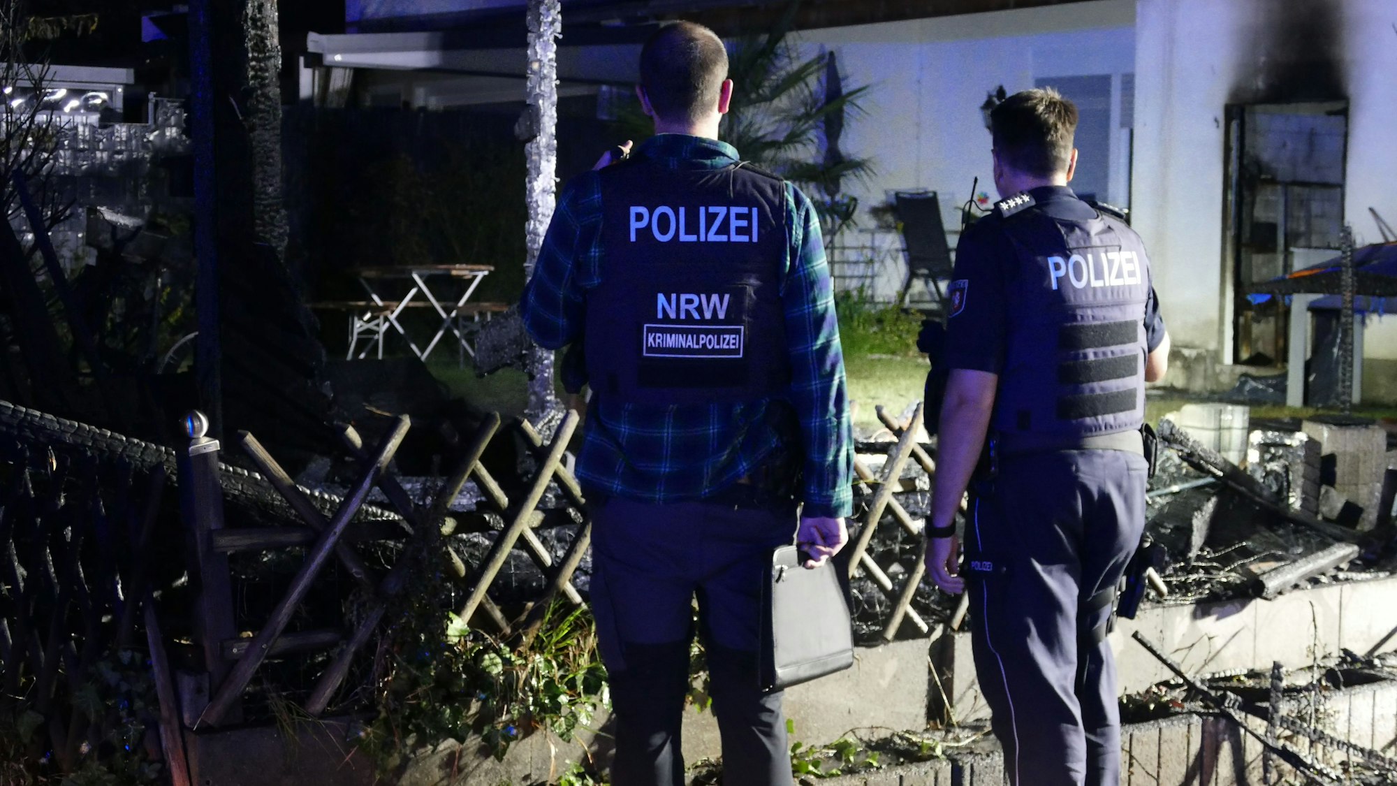 Polizisten der Kripo begutachten die Brandstelle. Von der Hütte sind nur verkohlte Reste übrig.