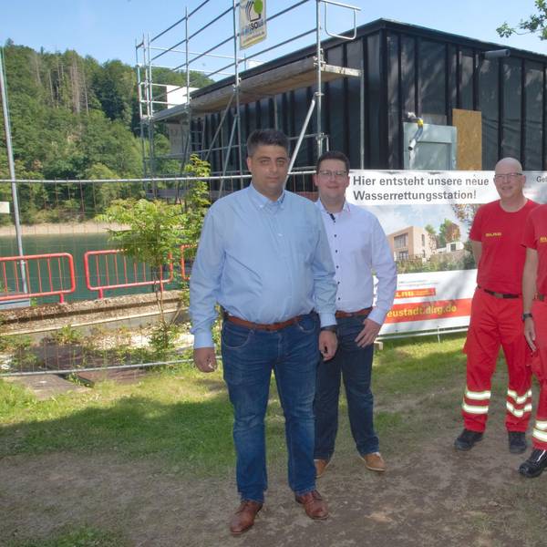 Vier Mitglieder der DLRG stehen an der Aggertalsperre vor einem Rohbau.