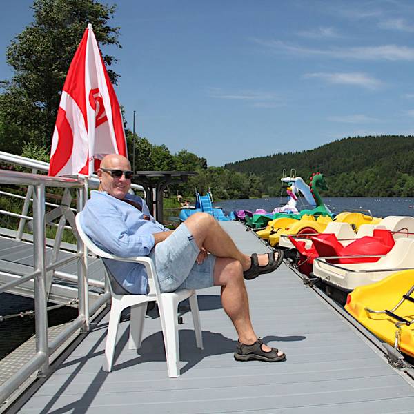 Das Bild zeigt einen Mann in Shorts auf einem Steg, an dem Tretboote in verschiedenen Farben liegen.
