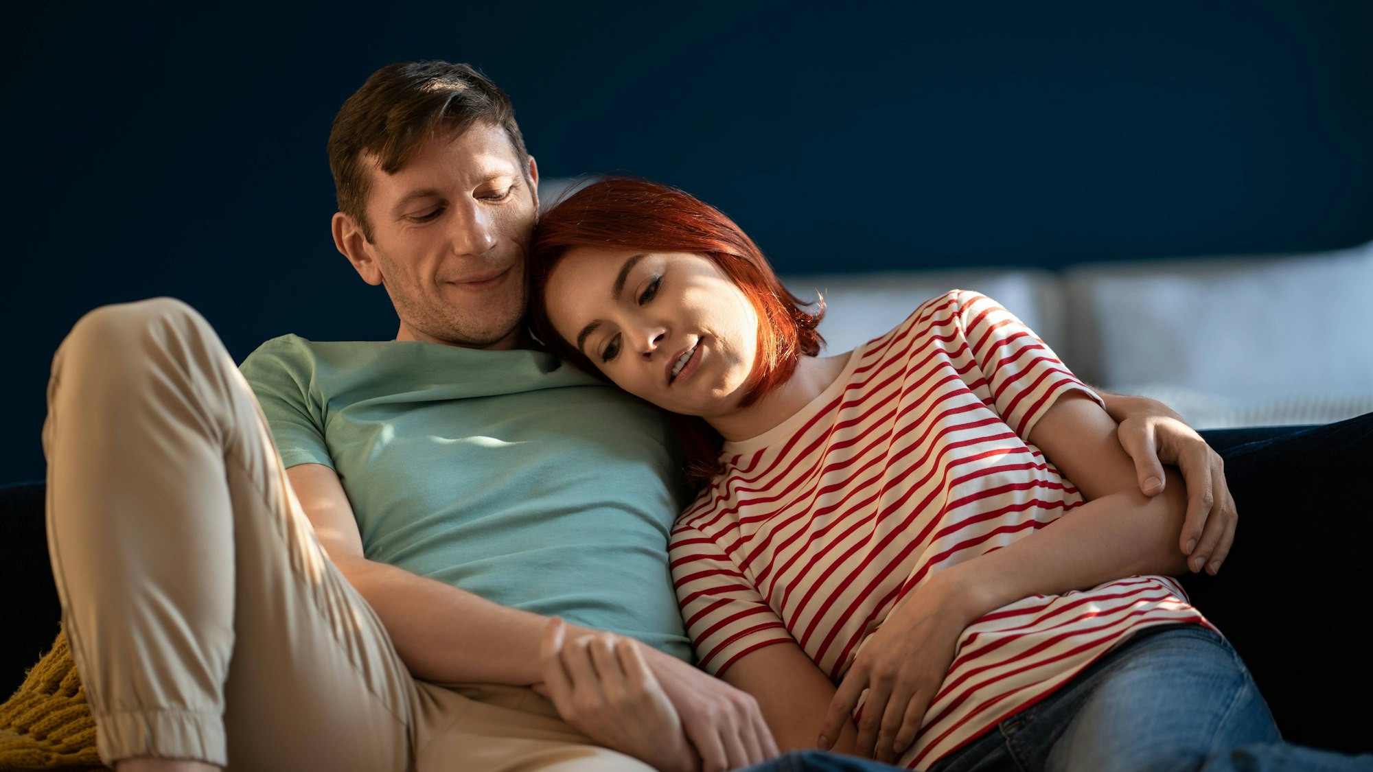 Verliebtes Paar sitzt auf der Couch und hält sich an den Händen, umarmt sich in der eigenen Wohnung