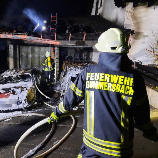 Ein Feuerwehrmann löscht zwei brennende Autos in einem Carport.