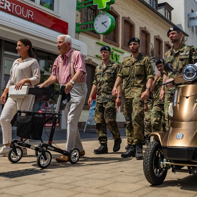 Soldaten in Feldanzügen marschieren auf der Neustraße. Vor ihnen ein Ex-Soldat mit Rollator und ein weiterer mit grünem Barett auf einem Elektromobil.