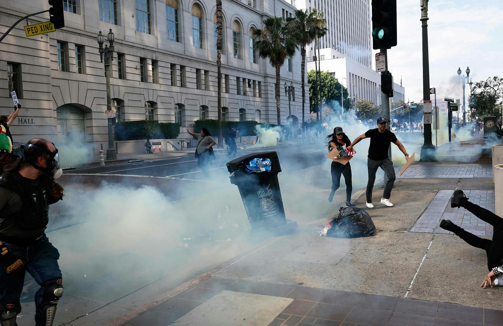 LOS ANGELES, CALIFORNIA - JUNE 14: Protesters run from tear gas as police clear a street of demonstrators in front of City Hall after an "unlawful assembly" was declared on June 14, 2025 in Los Angeles, California. Protesters held an anti-Trump "No Kings" Day demonstration in downtown Los Angeles which has been the focus of protests against Trump's immigration raids. Marches and protests against the Trump administration and its policies are taking place across the United States today. Protesters are also reacting in opposition to a planned military parade celebrating the 250th anniversary of the U.S. Army in Washington, DC, coinciding with President Trump's birthday. Mario Tama/Getty Images/AFP (Photo by MARIO TAMA / GETTY IMAGES NORTH AMERICA / Getty Images via AFP)
