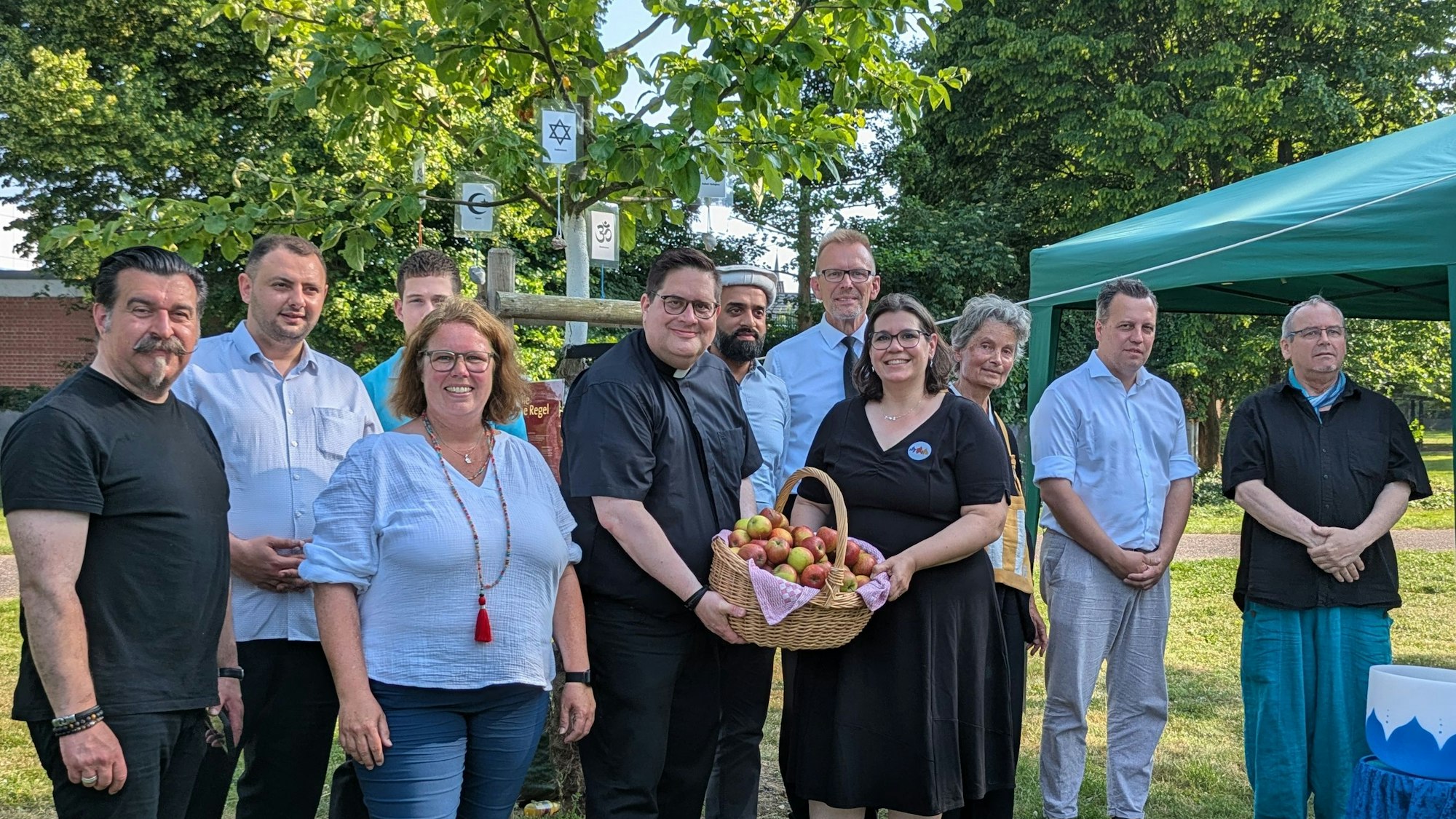 Die Vortragenden und die Organisatoren haben sich zum Foto unter dem Friedensbaum aufgestellt. Im Baum hängen die Symbole der Religionsgemeinschaften.