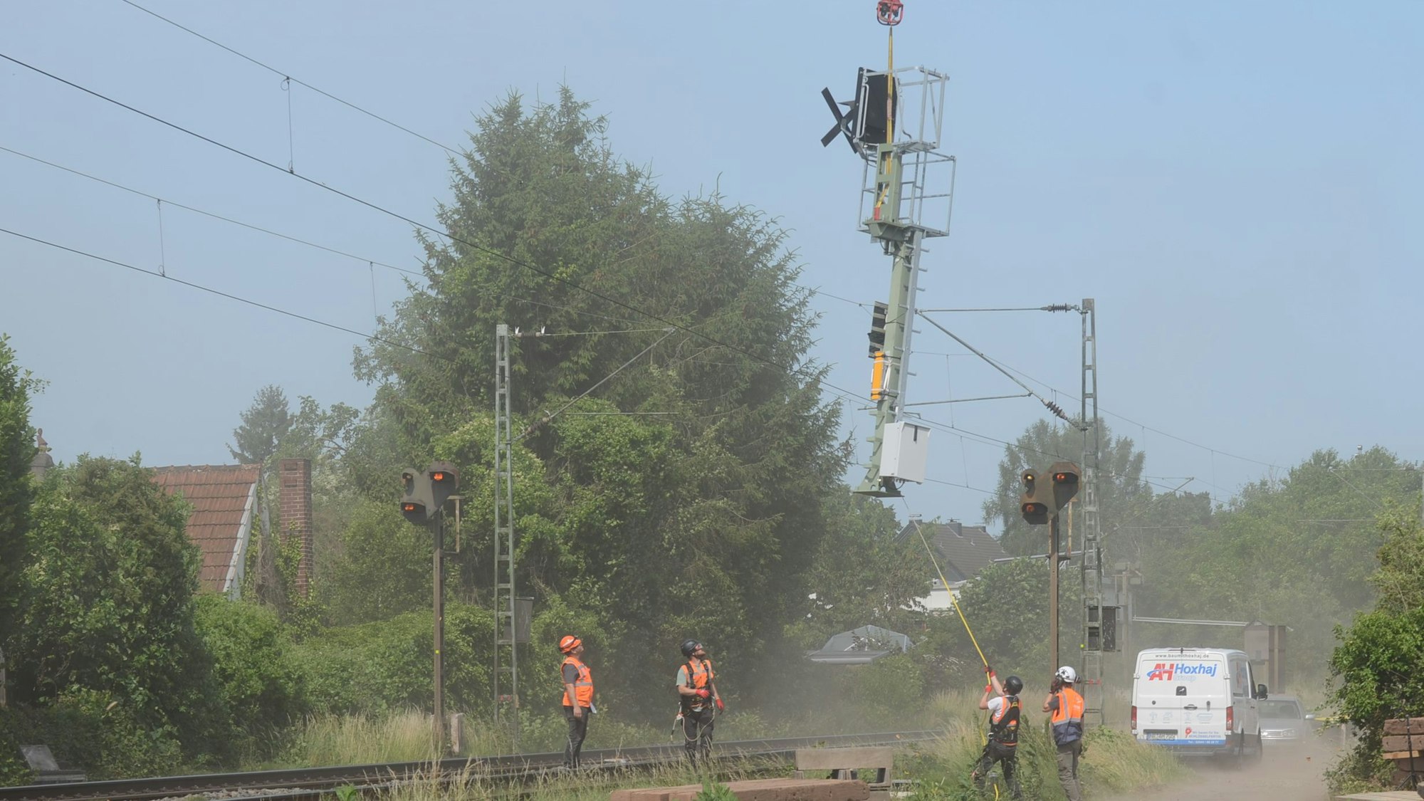 Männer mit Helm und Warnweste an einer Baustelle. Von einem Hubschrauber werden Masten für Signale herabgelassen.