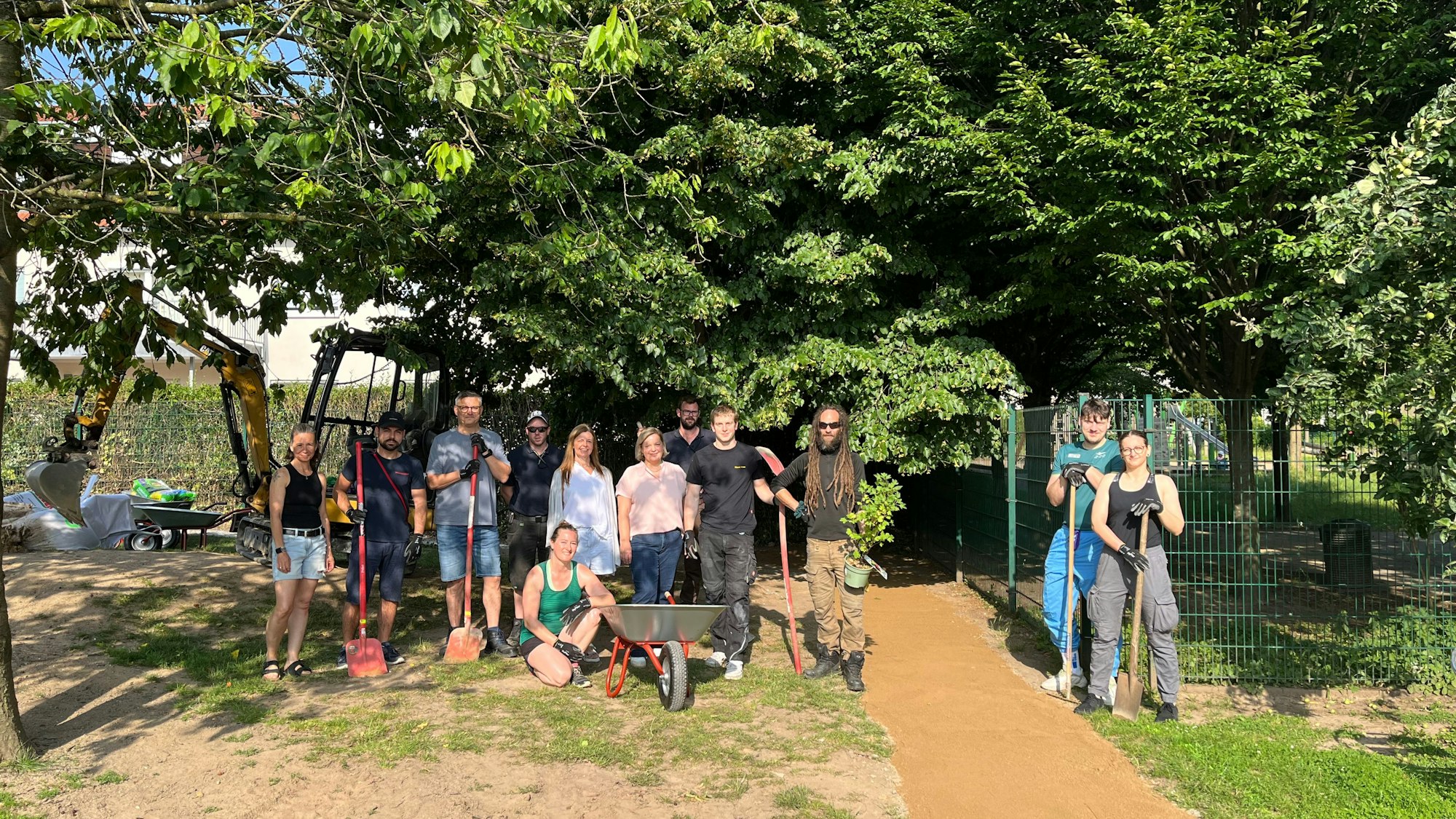 Zwölf Frauen und Männer aus verschiedenen Abteilungen des Flughafen Köln/Bonn stehen auf der Baustelle für eine Bobbycar-Strecke einer Kita.