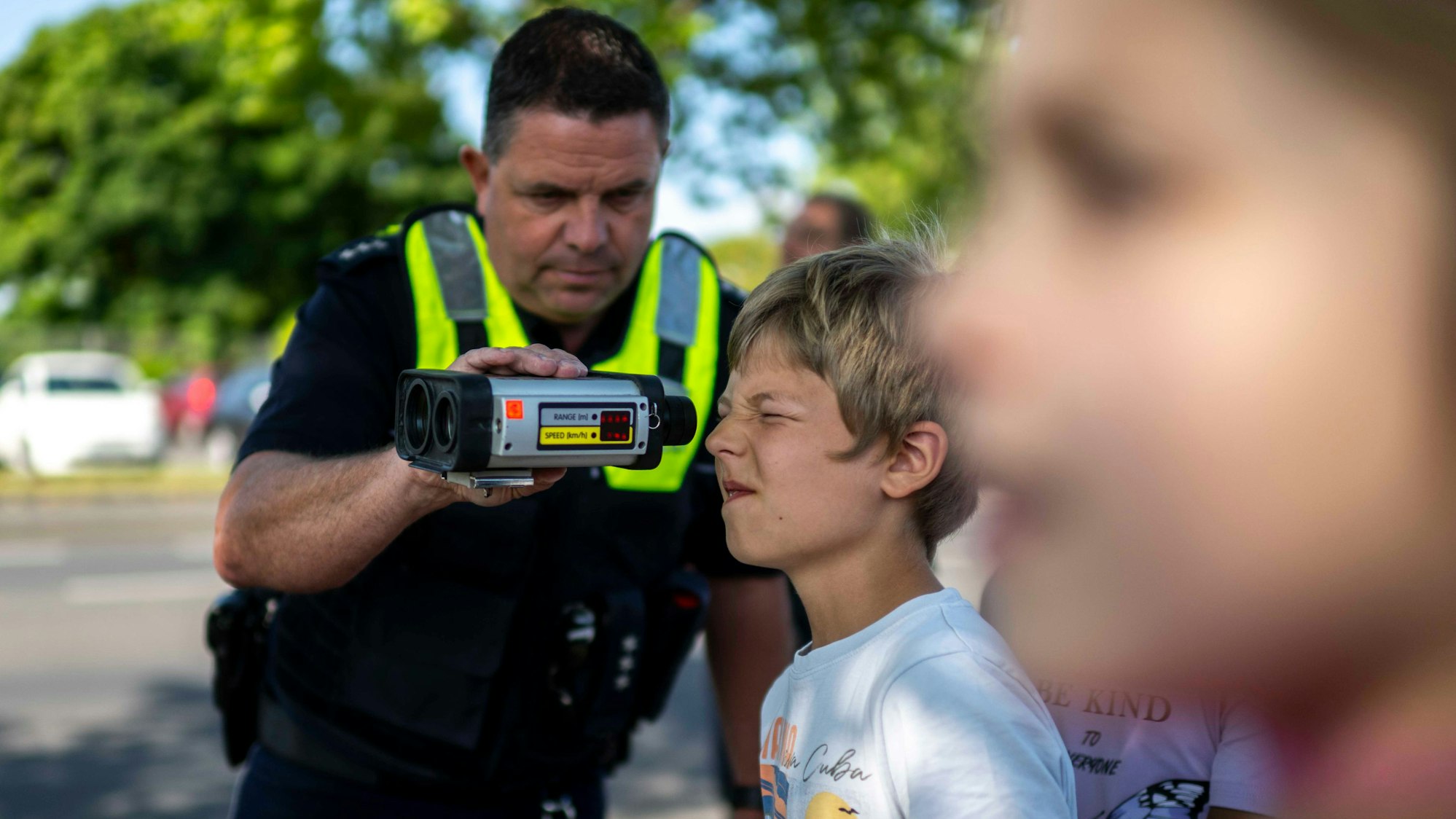 Das Bild zeigt einen Schüler, der mithilfe eines Polizisten durch ein Lasergerät schaut.