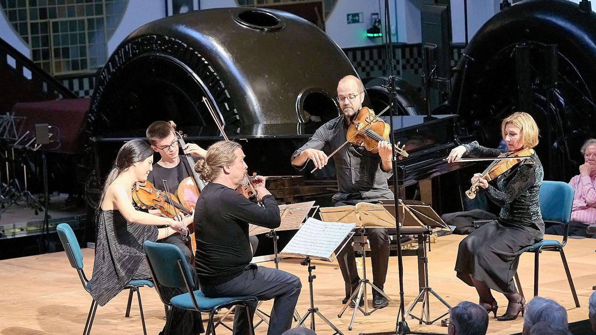 Zwei Musikerinnen und drei Musiker sitzen mit ihren Streichinstrumenten auf der Bühne des Jugendstilkraftwerks in Heimbach.