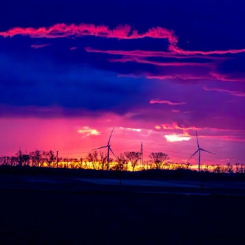 Ein Gewitter im Sonnenuntergang über dem Rhein-Erft-Kreis/Kreis Euskirchen. Im Sonnenuntergang drehen sich am Horizont Windräder.